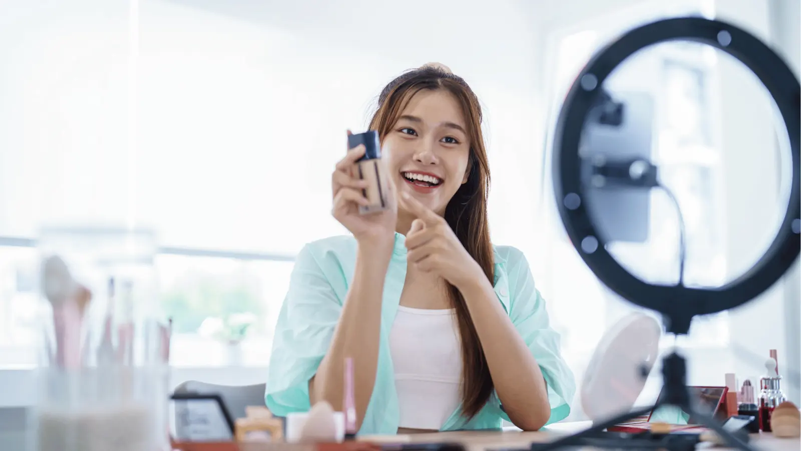 Young woman vlogger holding foundation bottle while filming with ring light for AI-assisted workflow
