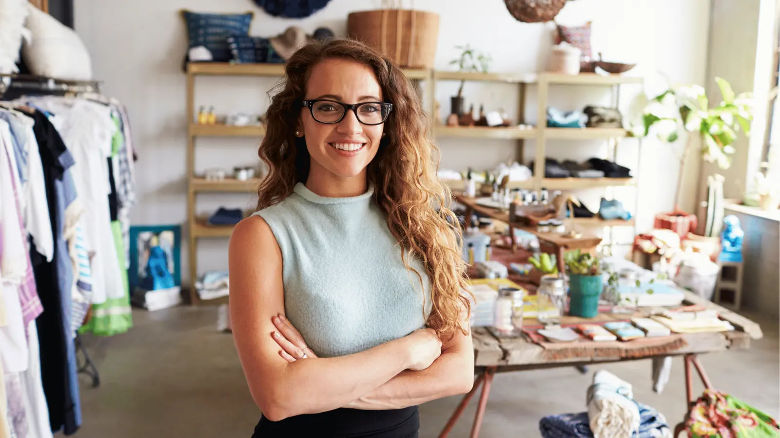 Smiling woman with glasses standing in boutique with arms crossed