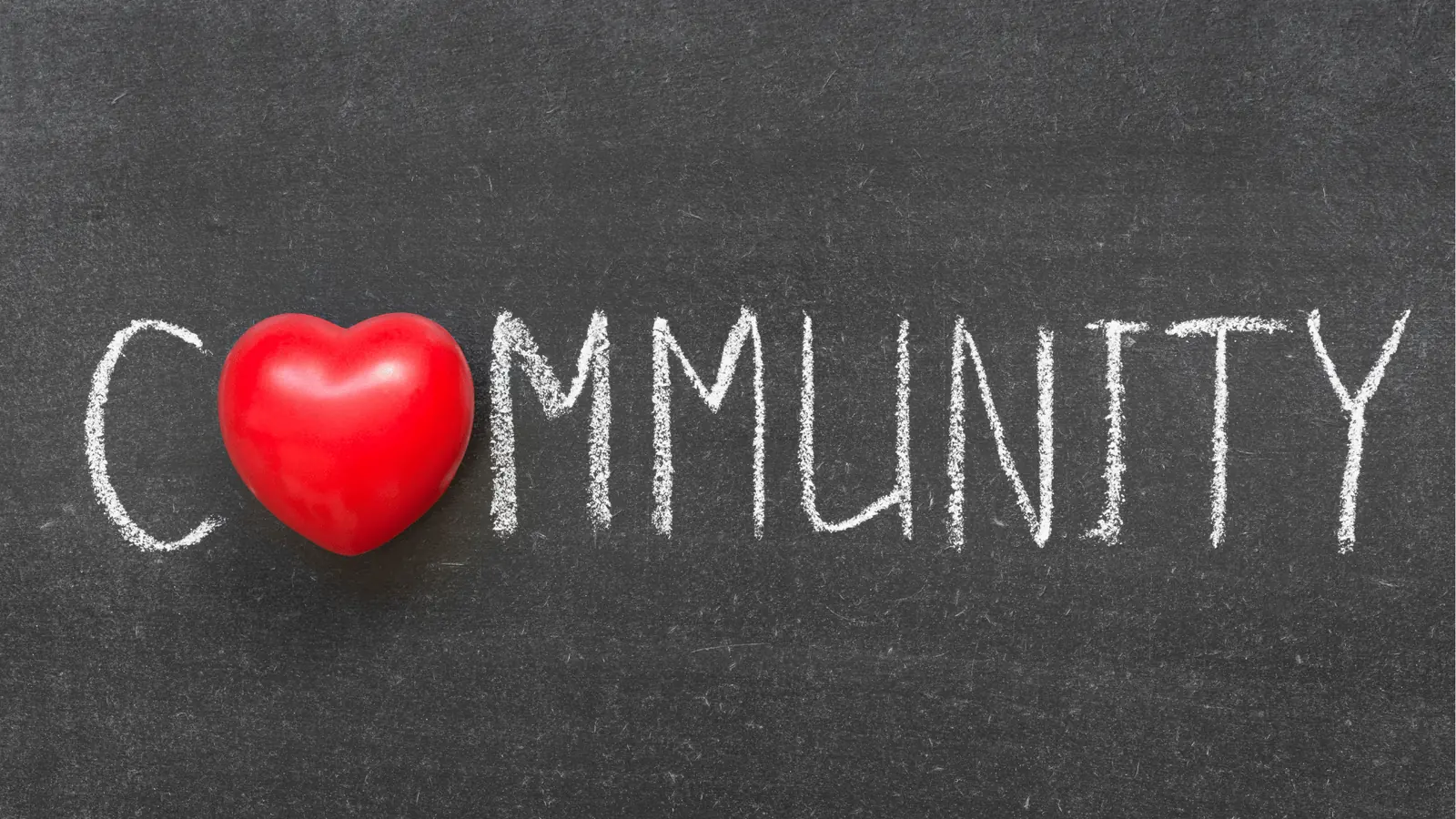 Red heart placed on a chalkboard spelling the word community in chalk
