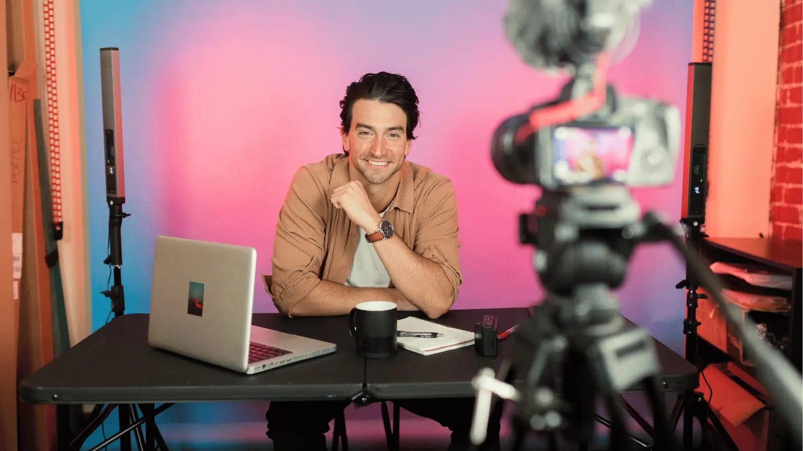 Smiling content creator sits at desk recording a video with camera