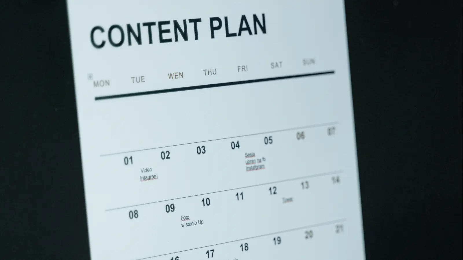 Tilted printed monthly content plan calendar page on dark background