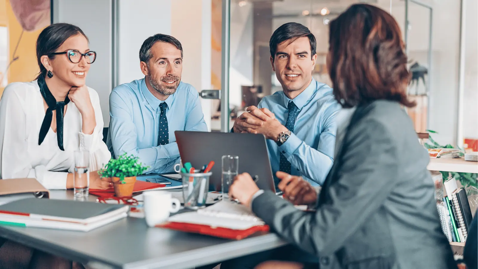 Four colleagues in a bright office meeting around a laptop and documents