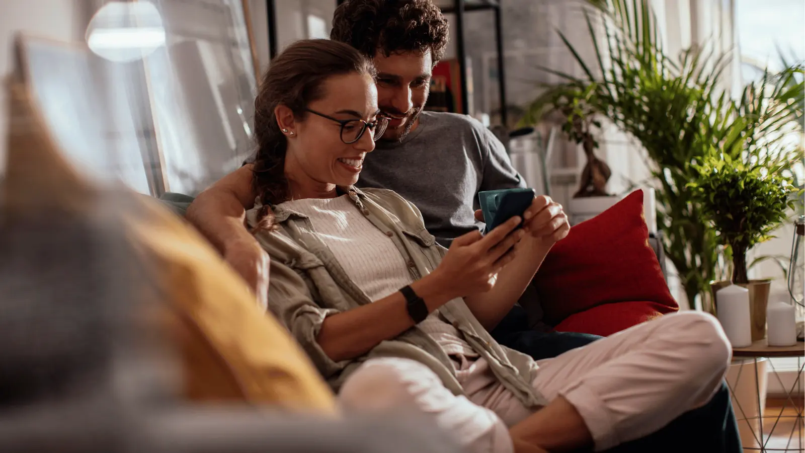 Smiling couple sitting on sofa looking at smartphone together in living room