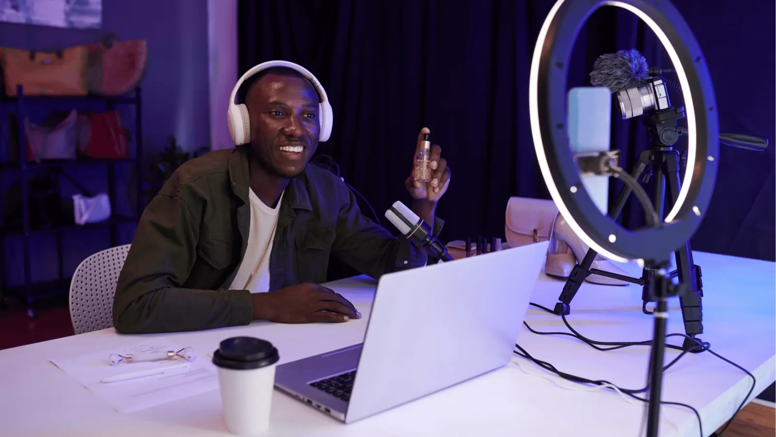 Smiling man with headphones holding a cosmetic bottle during a recording session for team collaboration