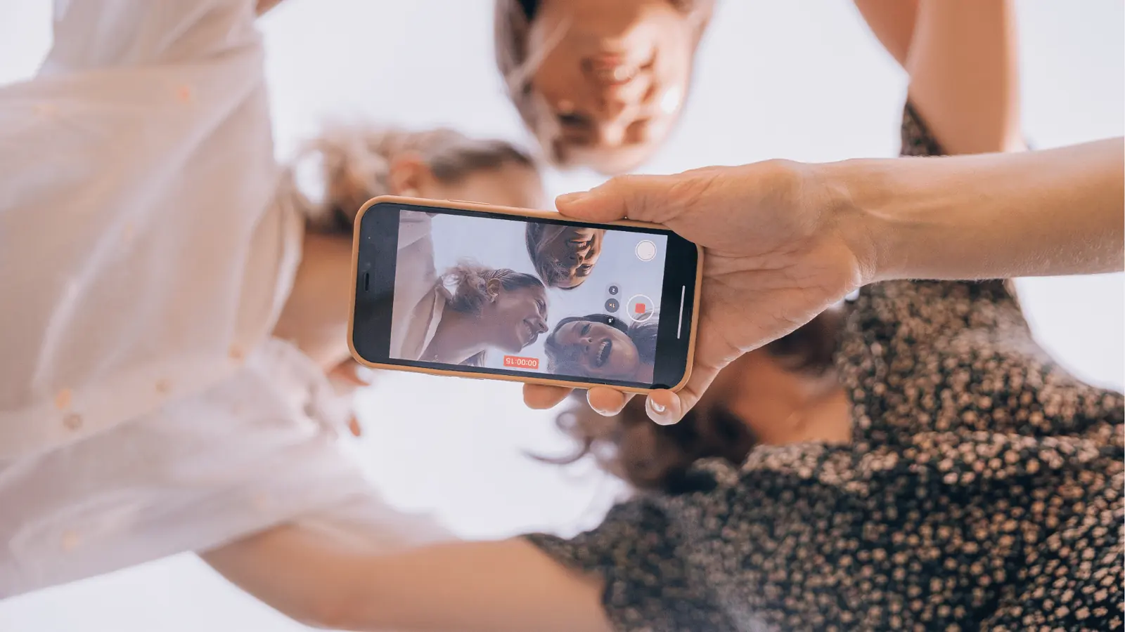 Group of friends smiling down at smartphone recording a selfie video