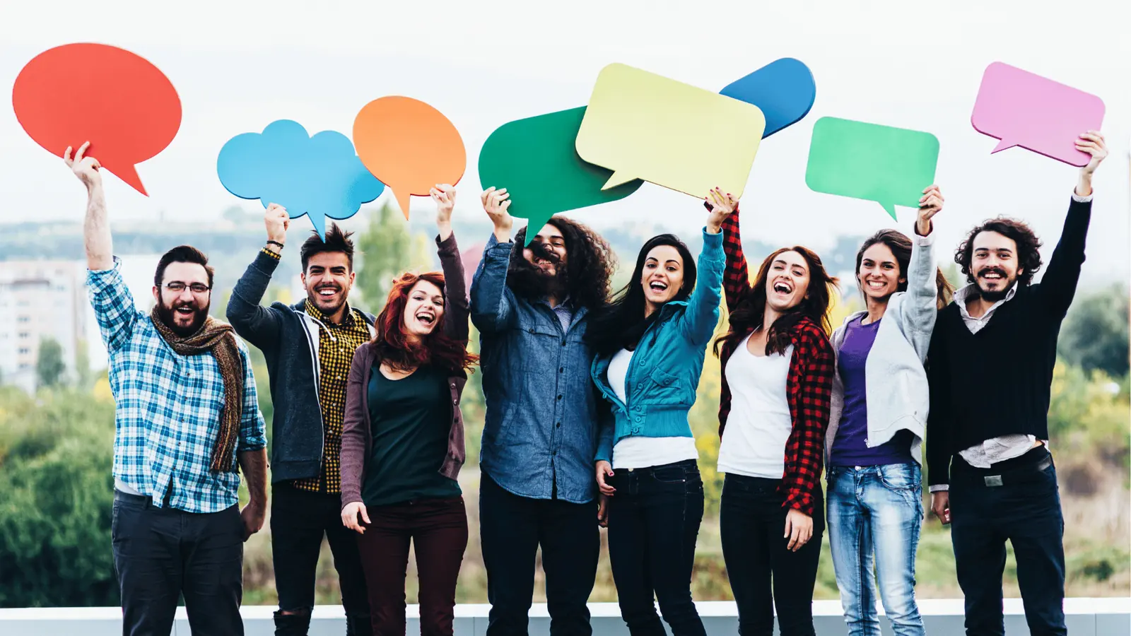 Diverse group of young adults holding colorful speech bubble signs outdoors