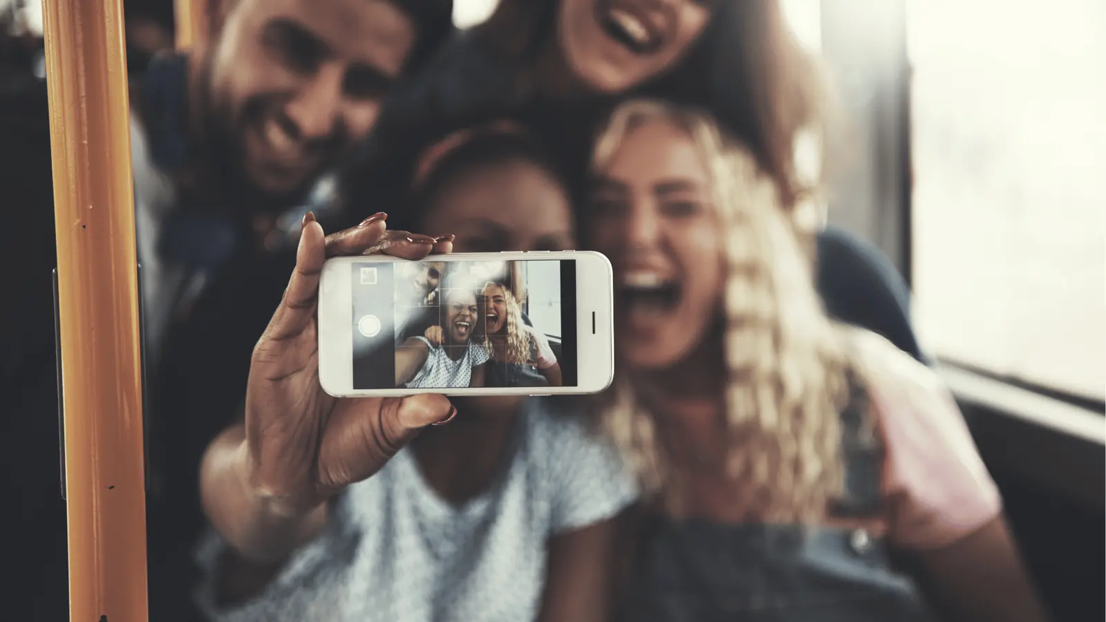 Hand holding smartphone showing four friends laughing together in a selfie