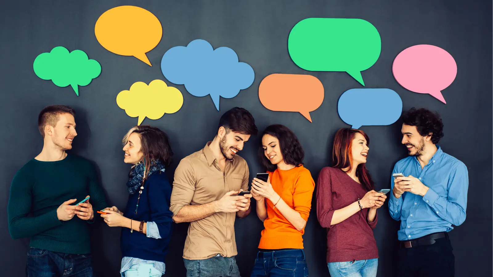 Six people standing against a wall smiling and using smartphones under colorful speech bubbles
