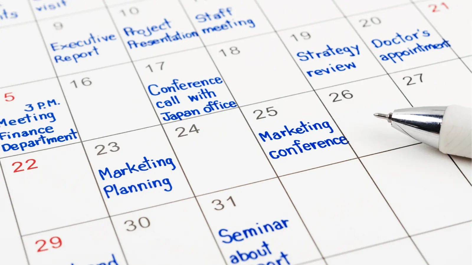 Close-up of paper calendar with blue handwritten meetings and a pen for scheduling