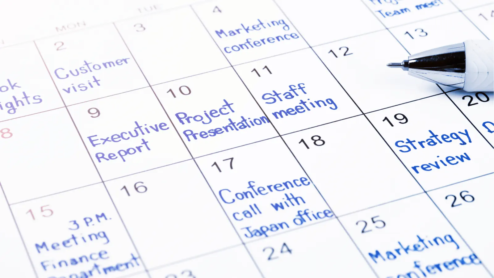 Close-up of monthly calendar with handwritten meetings and a pen