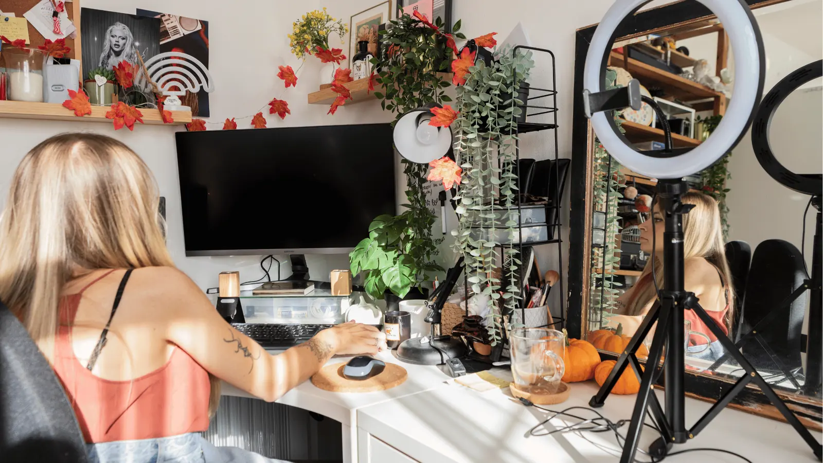 Woman at decorated home desk with ring light, monitor, plants, and pumpkins