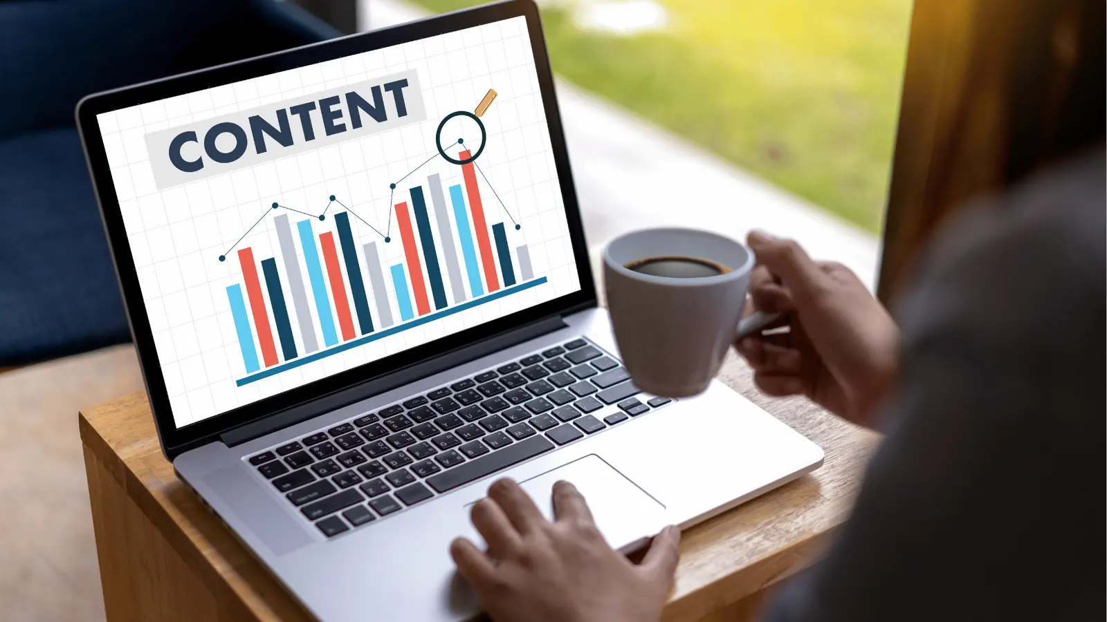 Person at laptop viewing content bar chart while holding a coffee cup