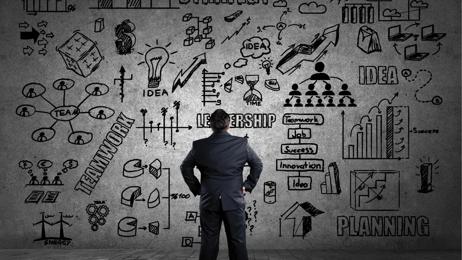 Man in suit facing concrete wall filled with business sketches and charts