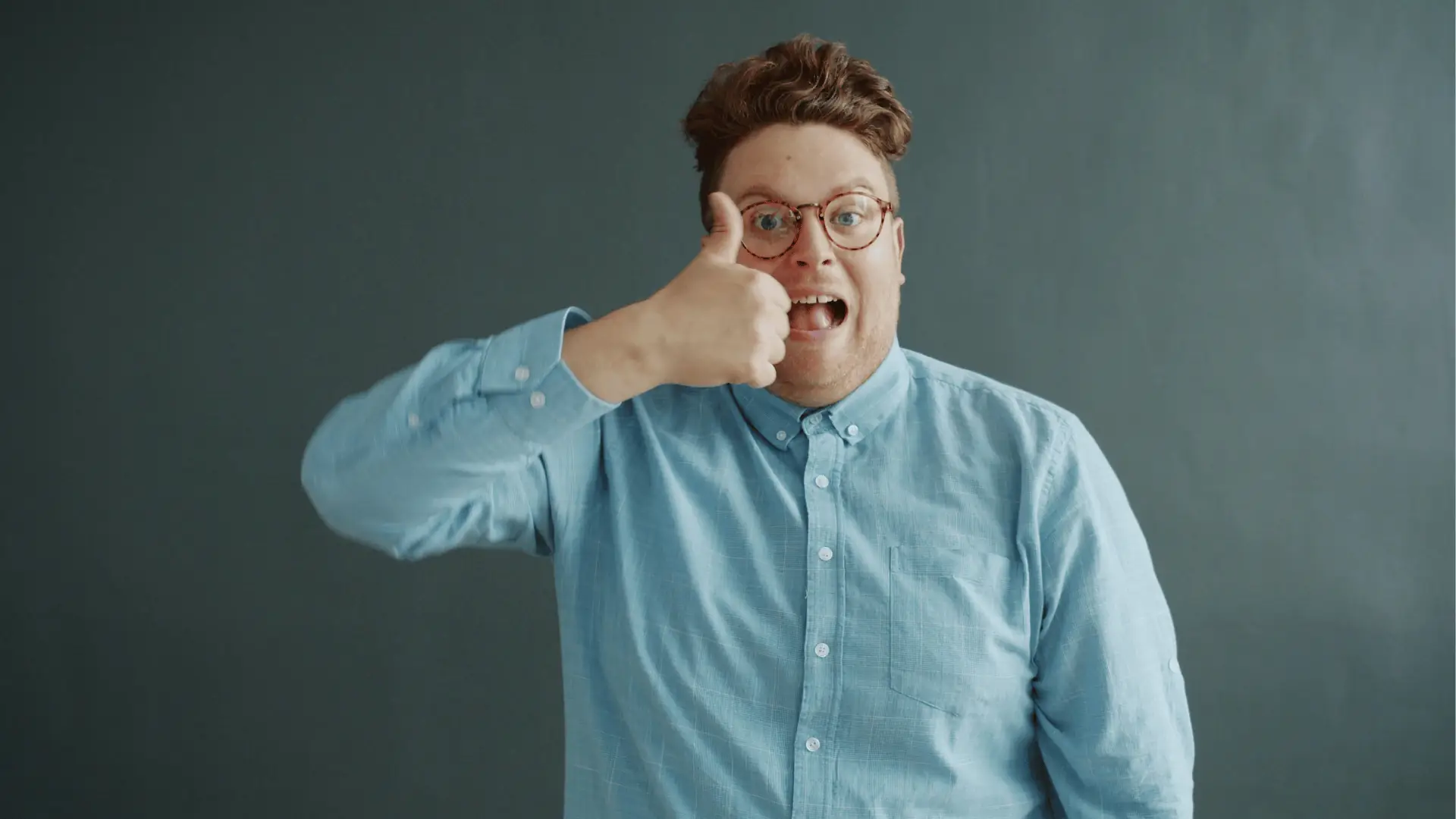 Man with glasses in blue shirt giving a thumbs-up and surprised expression