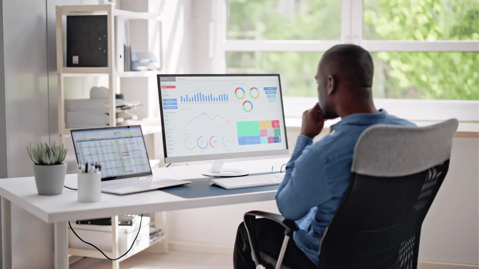 Man sitting at desk looking at analytics dashboards on dual monitors for approval workflow