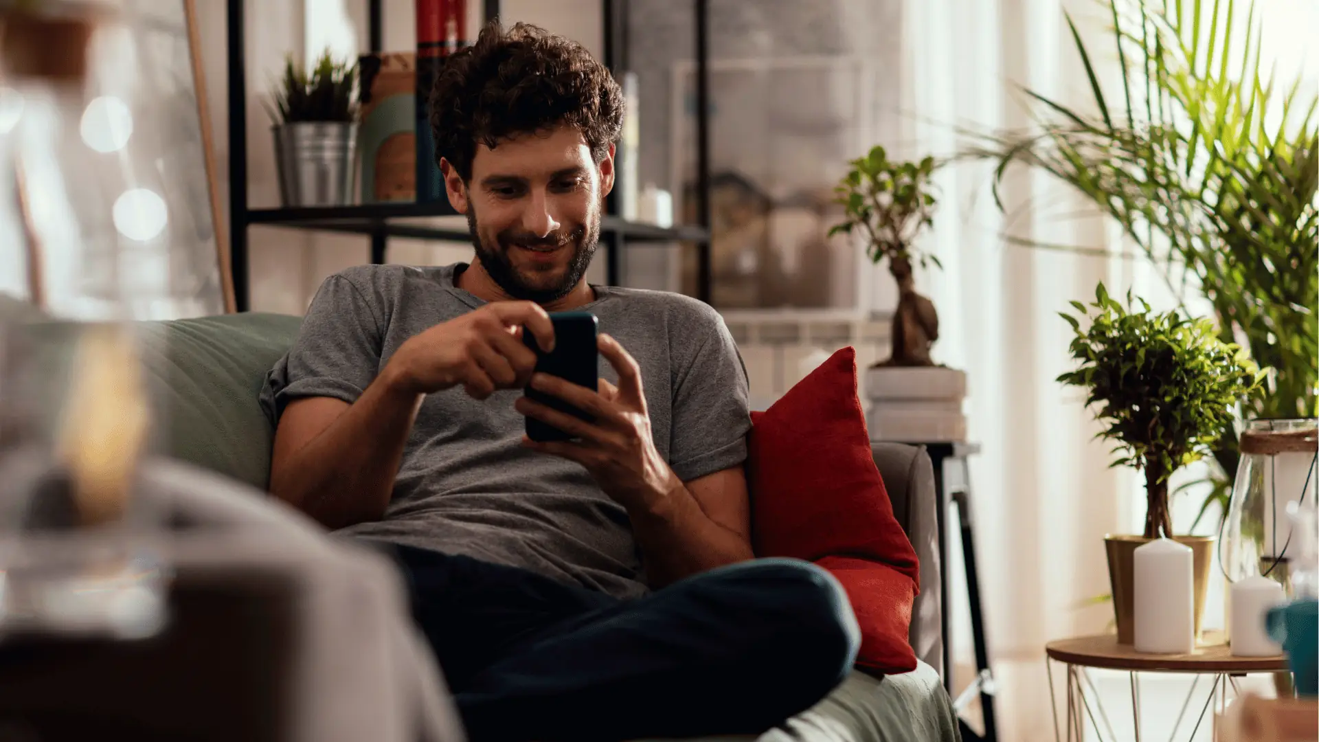 Smiling man sitting on sofa looking at smartphone in cozy living room