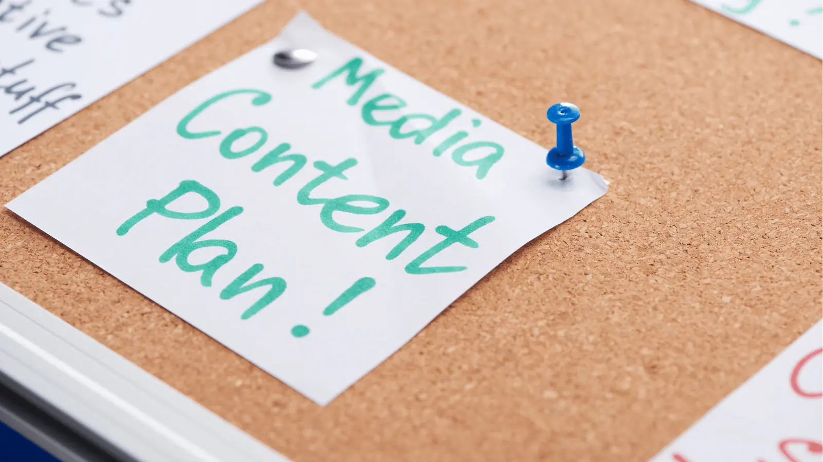 Close-up of corkboard with pinned note reading 'Media Content Plan!' and blue pushpin