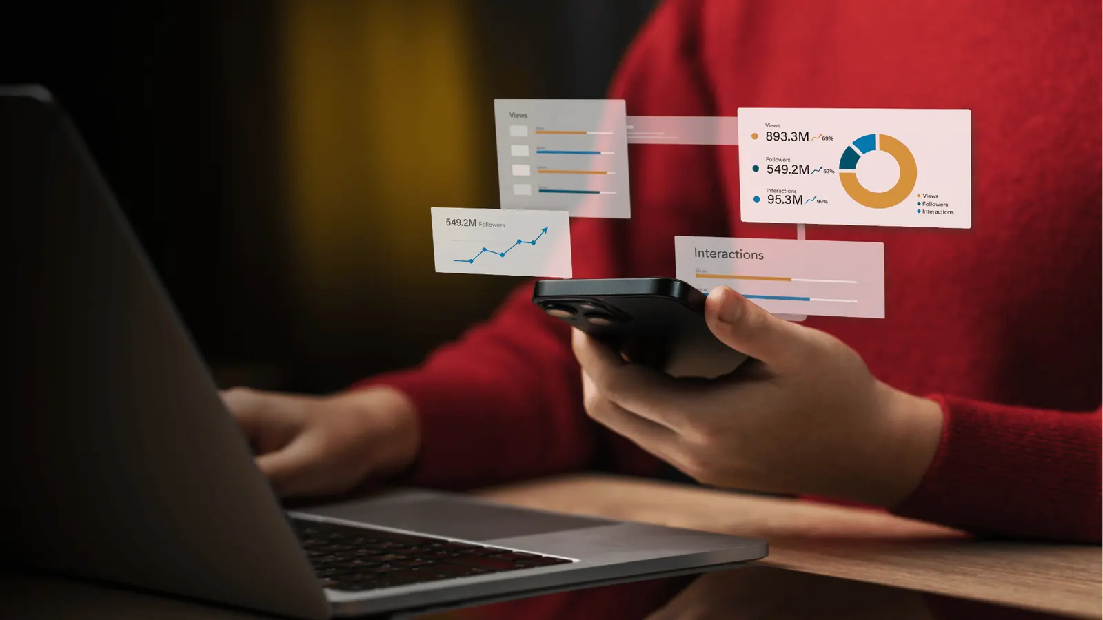 Person holding smartphone beside laptop with floating analytics charts