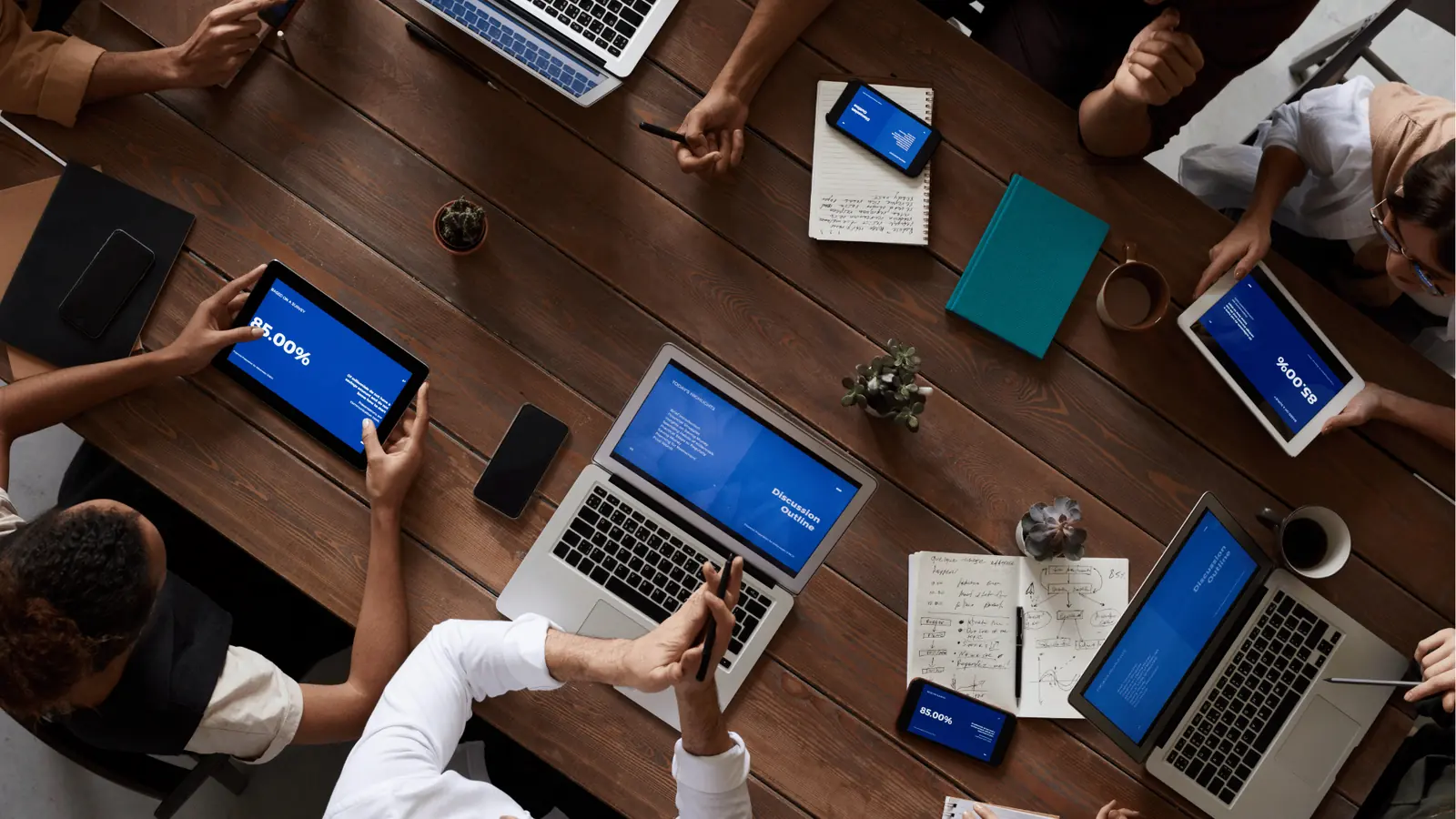 Overhead view of a team meeting with laptops, tablets, and notebooks on table