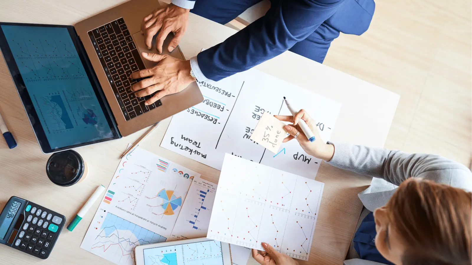 Overhead view of two people reviewing printed charts and a laptop