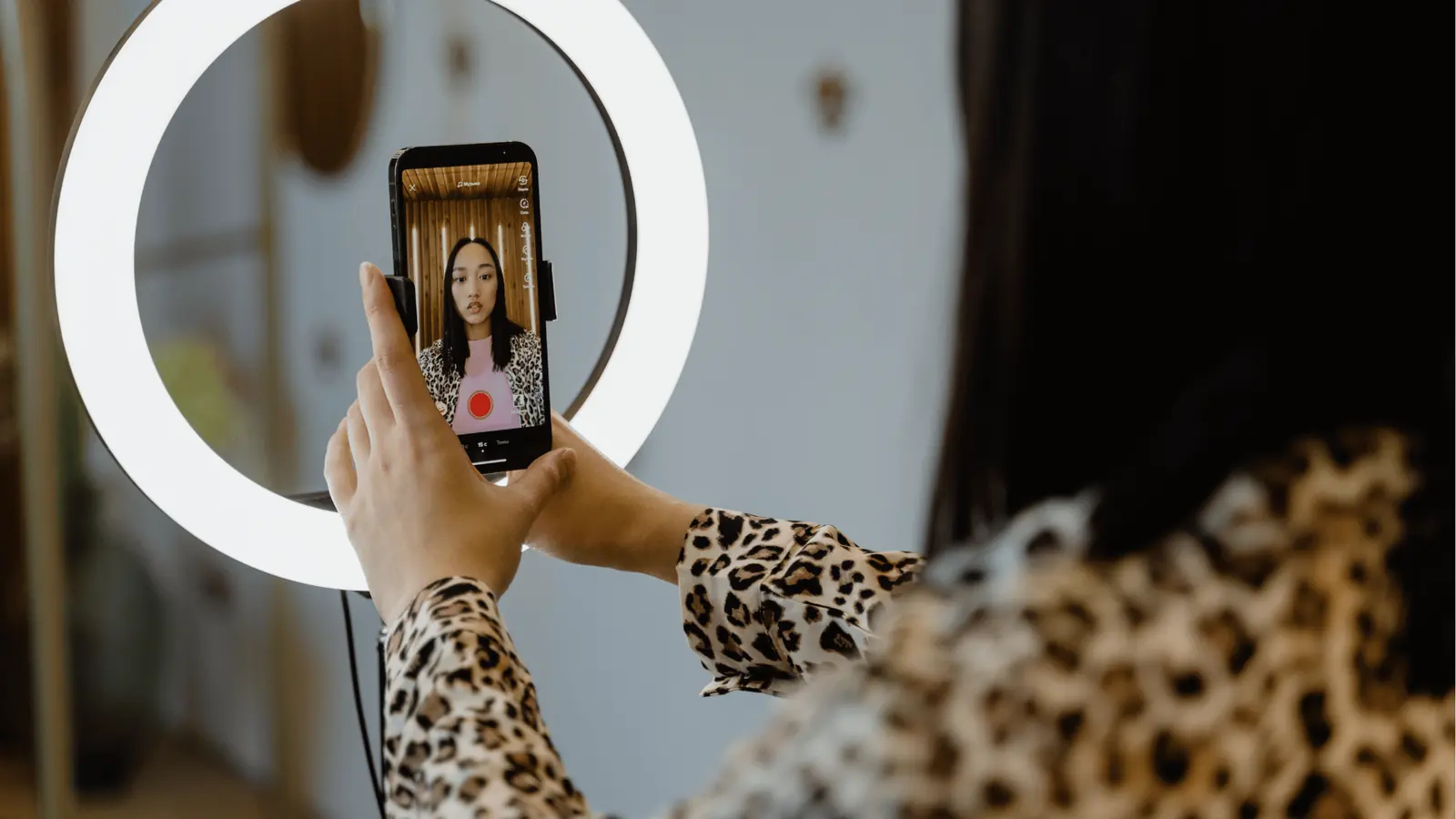 Person recording selfie video on smartphone held in ring light