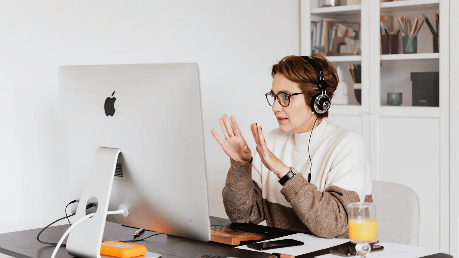 Person wearing headphones gesturing during a video call at desk