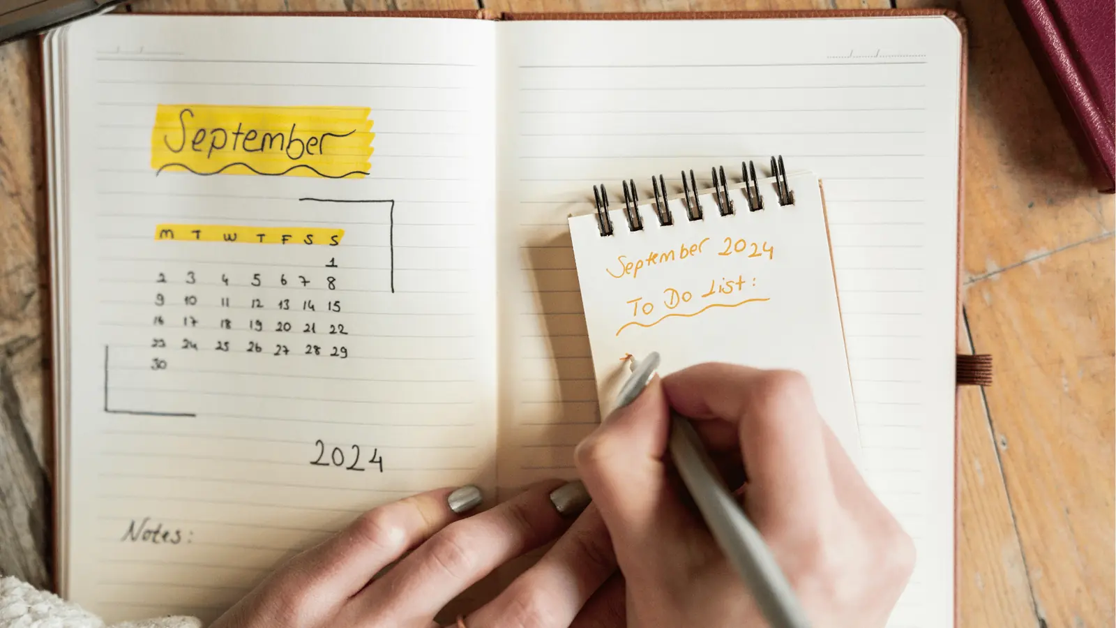 Person writing a September 2024 to-do list next to a notebook calendar