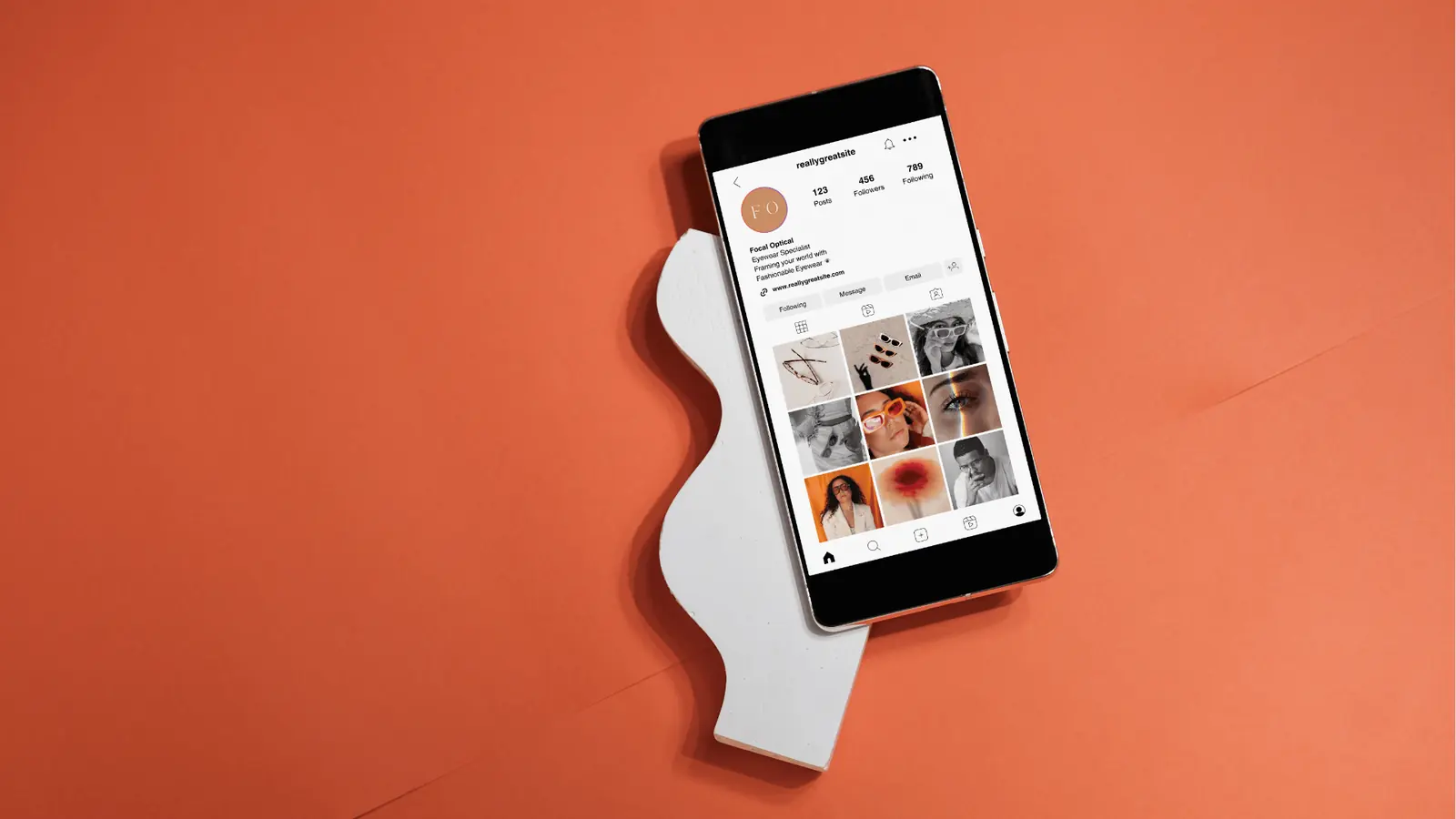 Smartphone displaying an Instagram profile grid on orange background with white prop