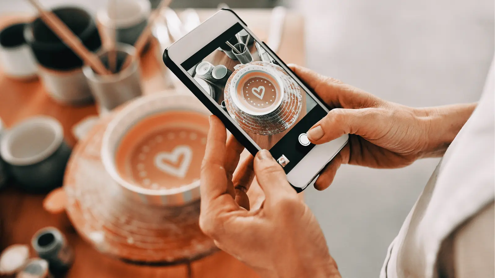 Hands holding phone photographing ceramic bowl with painted heart on top