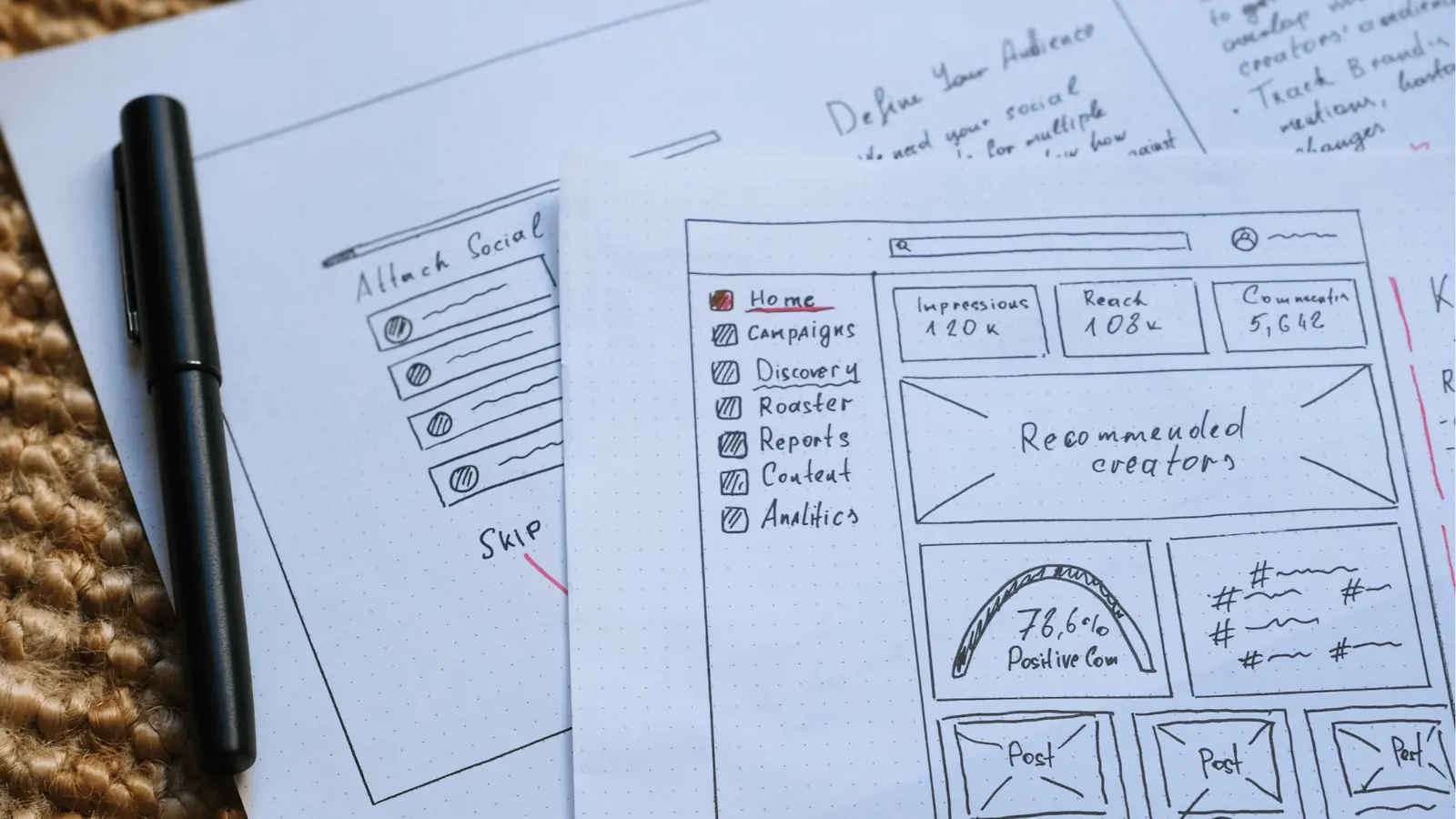 Top-down photo of hand-drawn social dashboard wireframe sketches with pen