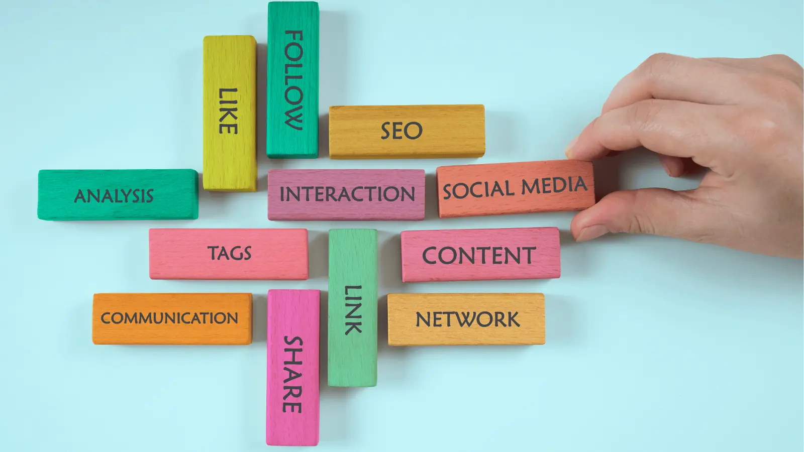 Hand arranging colorful wooden blocks labeled social media and content on blue background