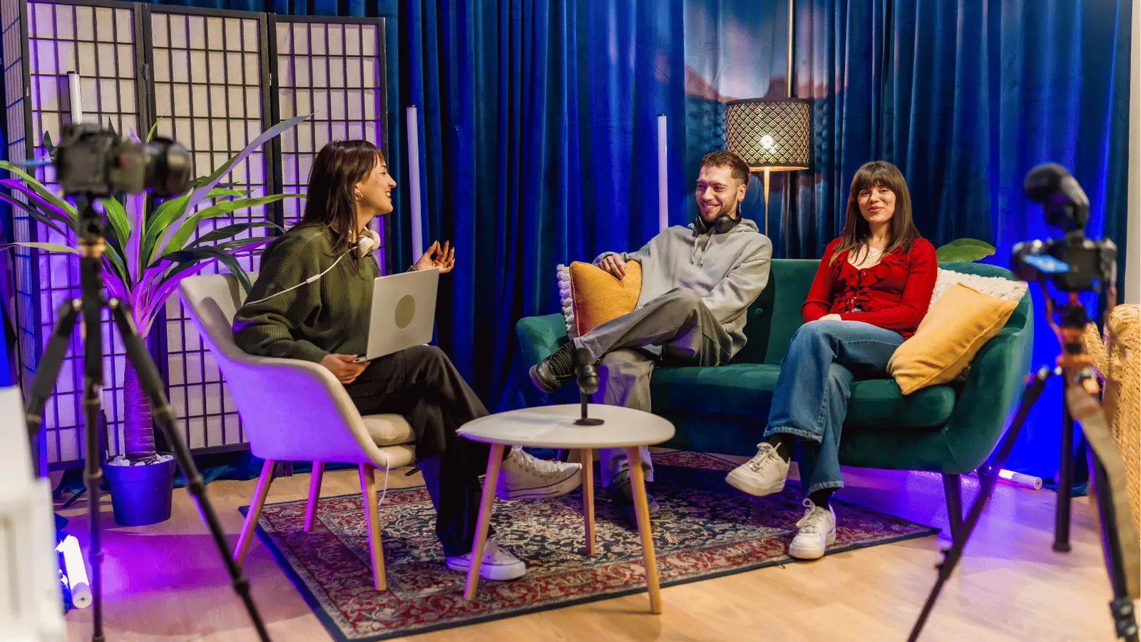Three people in a small studio set with cameras, laptop, and microphone