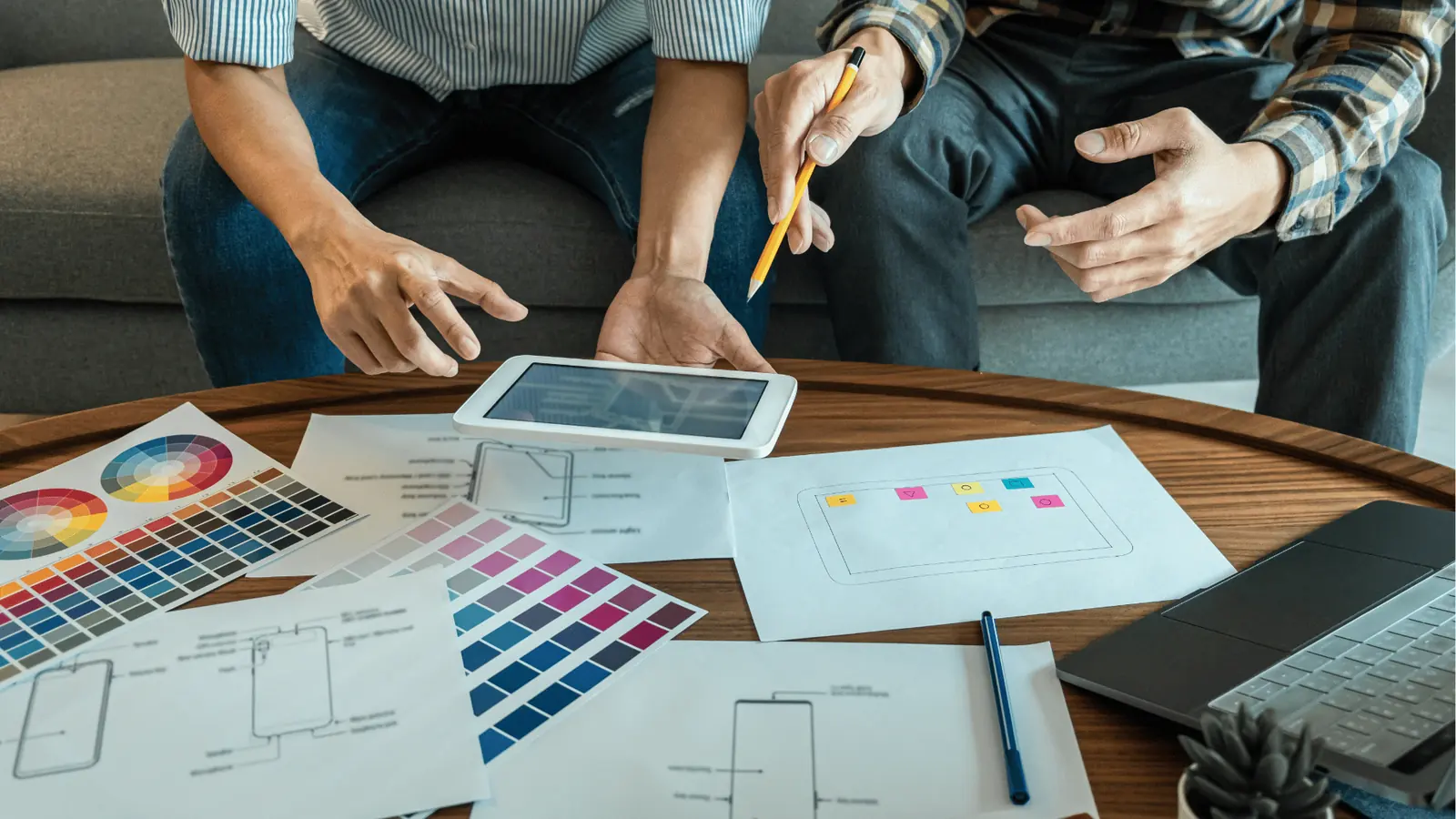 Two people reviewing tablet and printed wireframes on table with color swatches