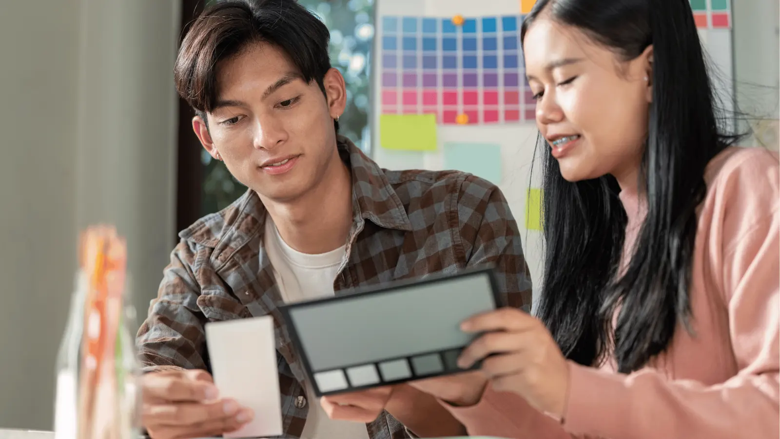 Two people comparing color swatches and a palette in a bright workspace