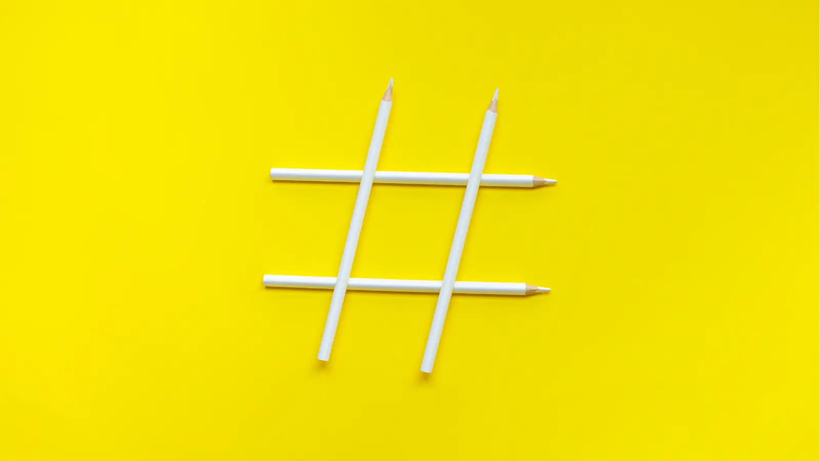 Four white pencils arranged as a hashtag on yellow background