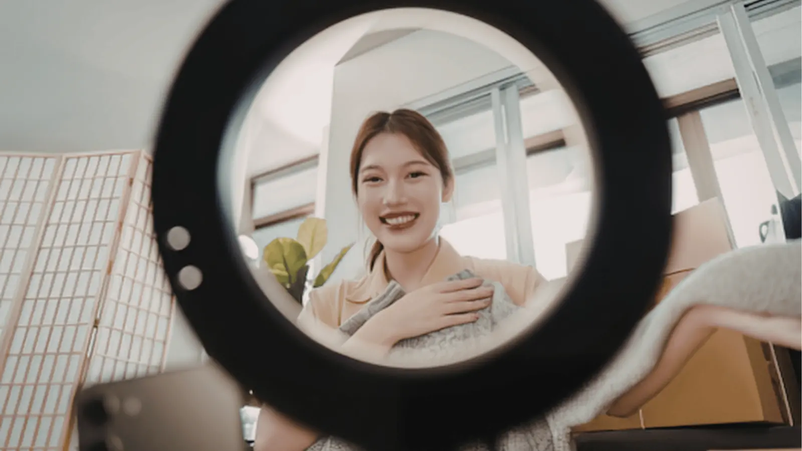 Young woman smiling at camera through ring light while holding a blanket