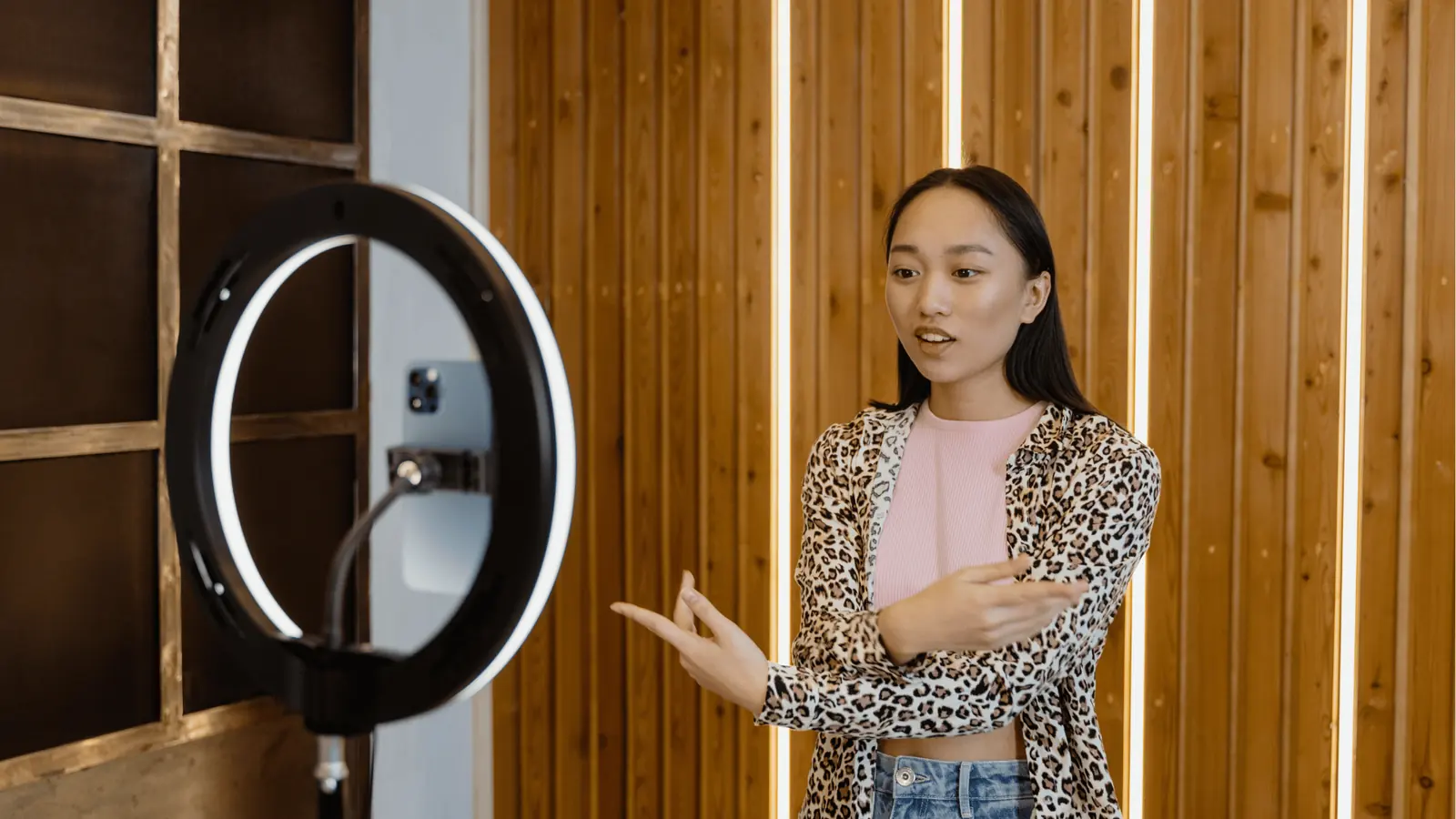 Young woman speaking to camera with ring light in wooden studio