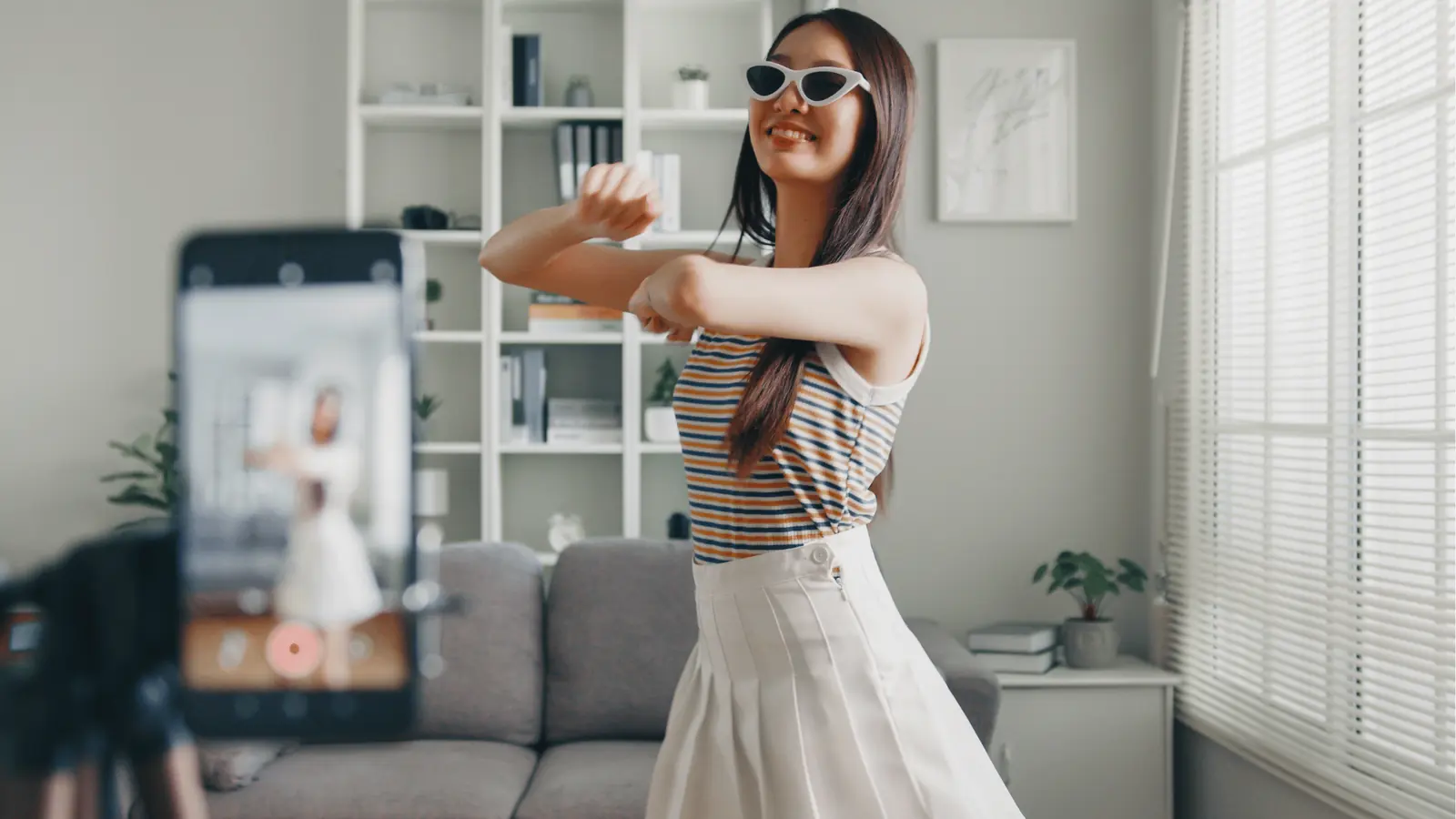 Young woman in sunglasses dancing while recording video in living room