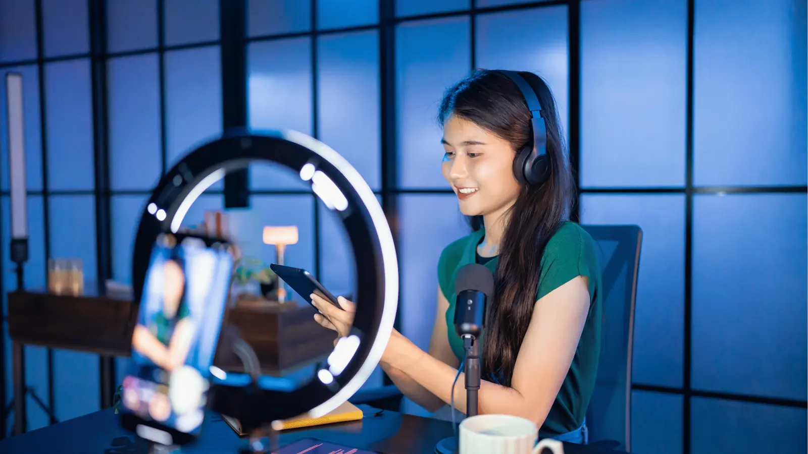 Young woman wearing headphones recording with tablet, ring light, and microphone