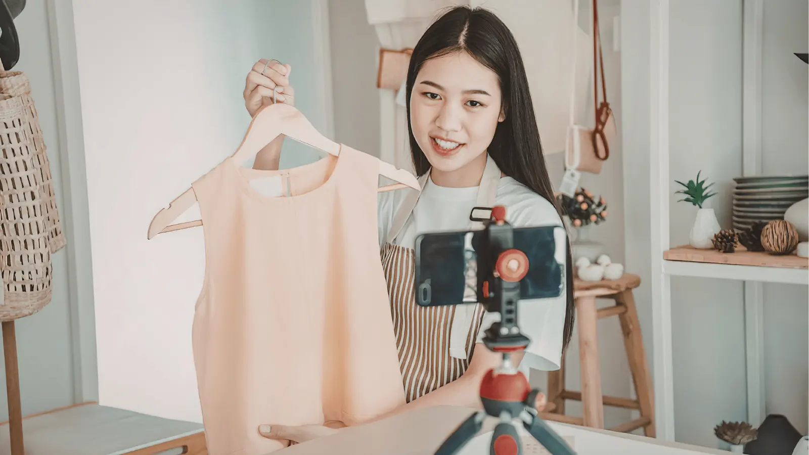 Young woman holding a peach dress on a hanger in front of smartphone camera for scheduling