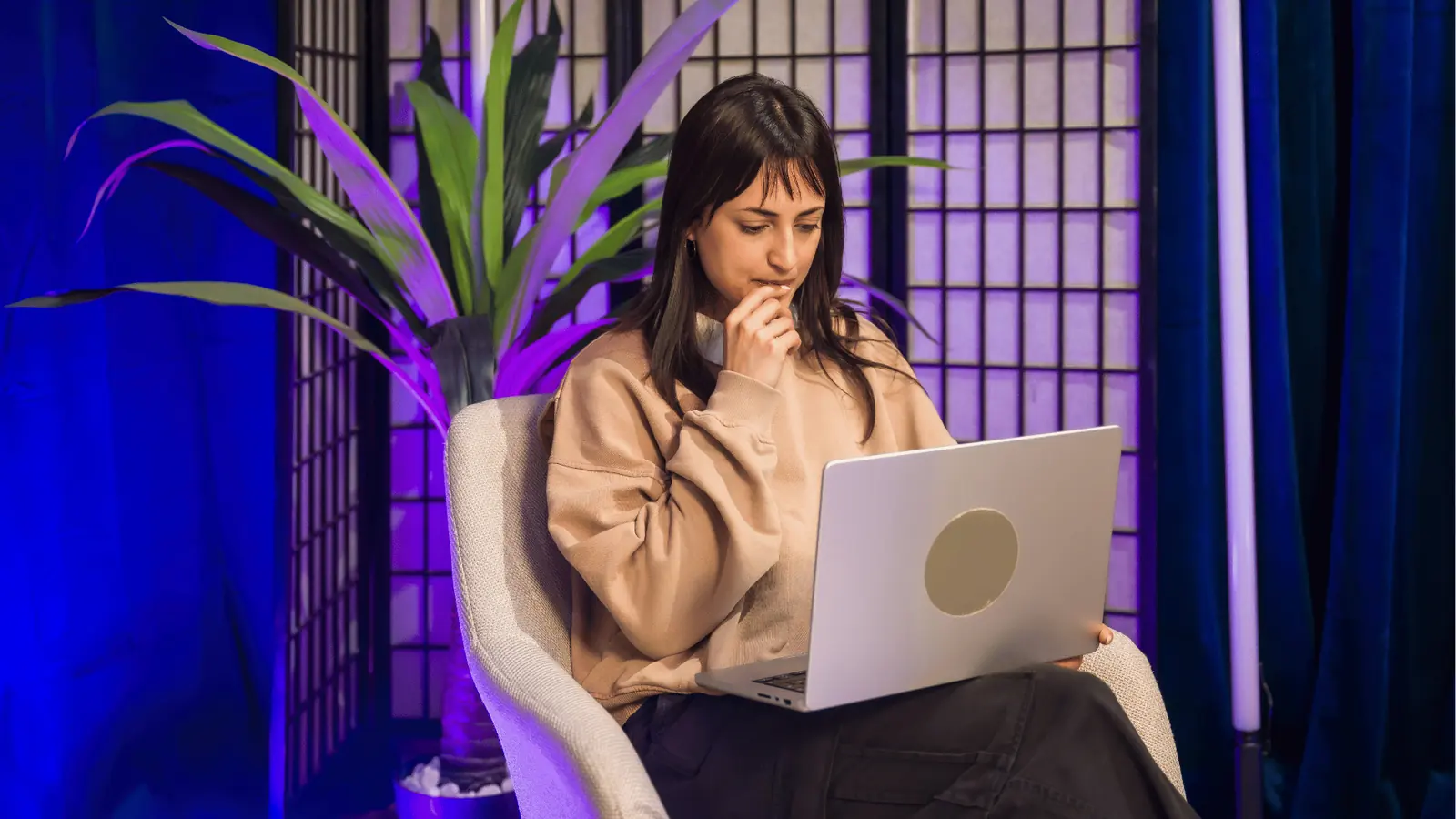 Young woman seated in armchair working on a laptop under purple lighting