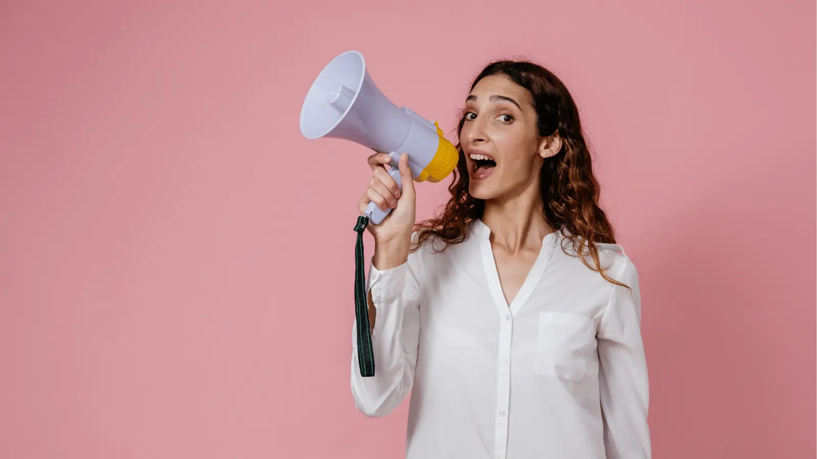 Woman in white shirt shouting into megaphone against pink background