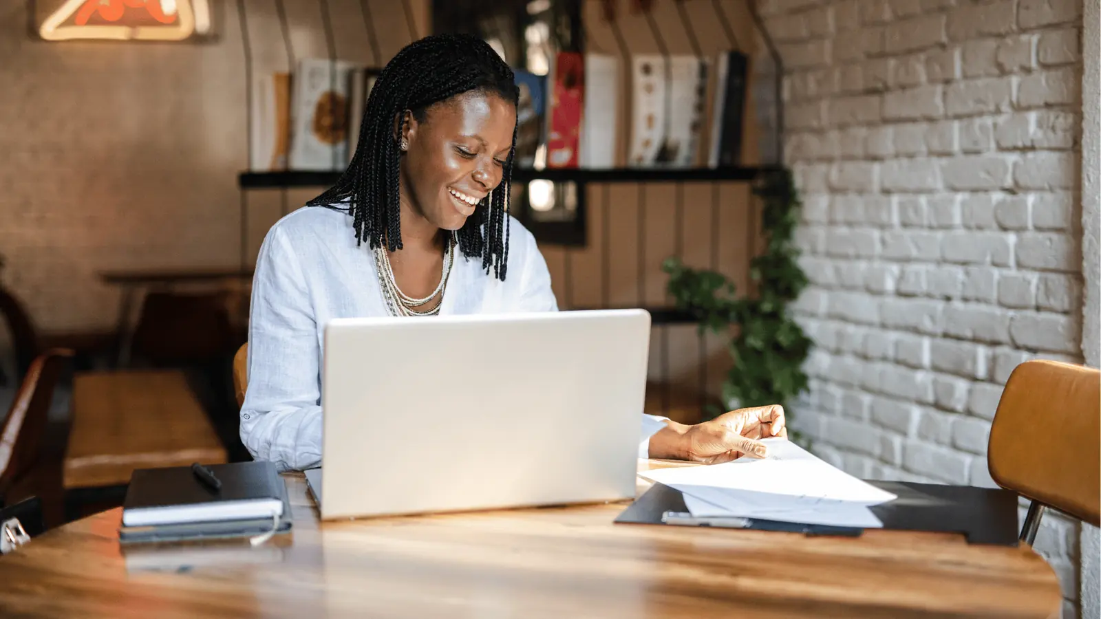 Woman smiling while working on laptop at a cafe table with papers