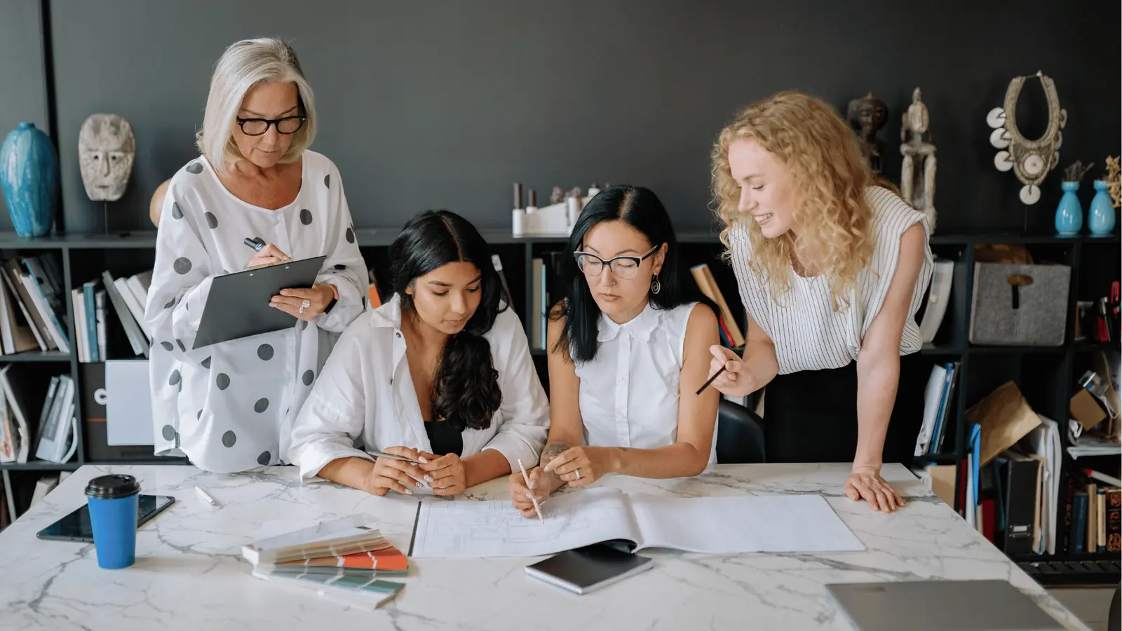 Four women reviewing design plans and color swatches at a studio table