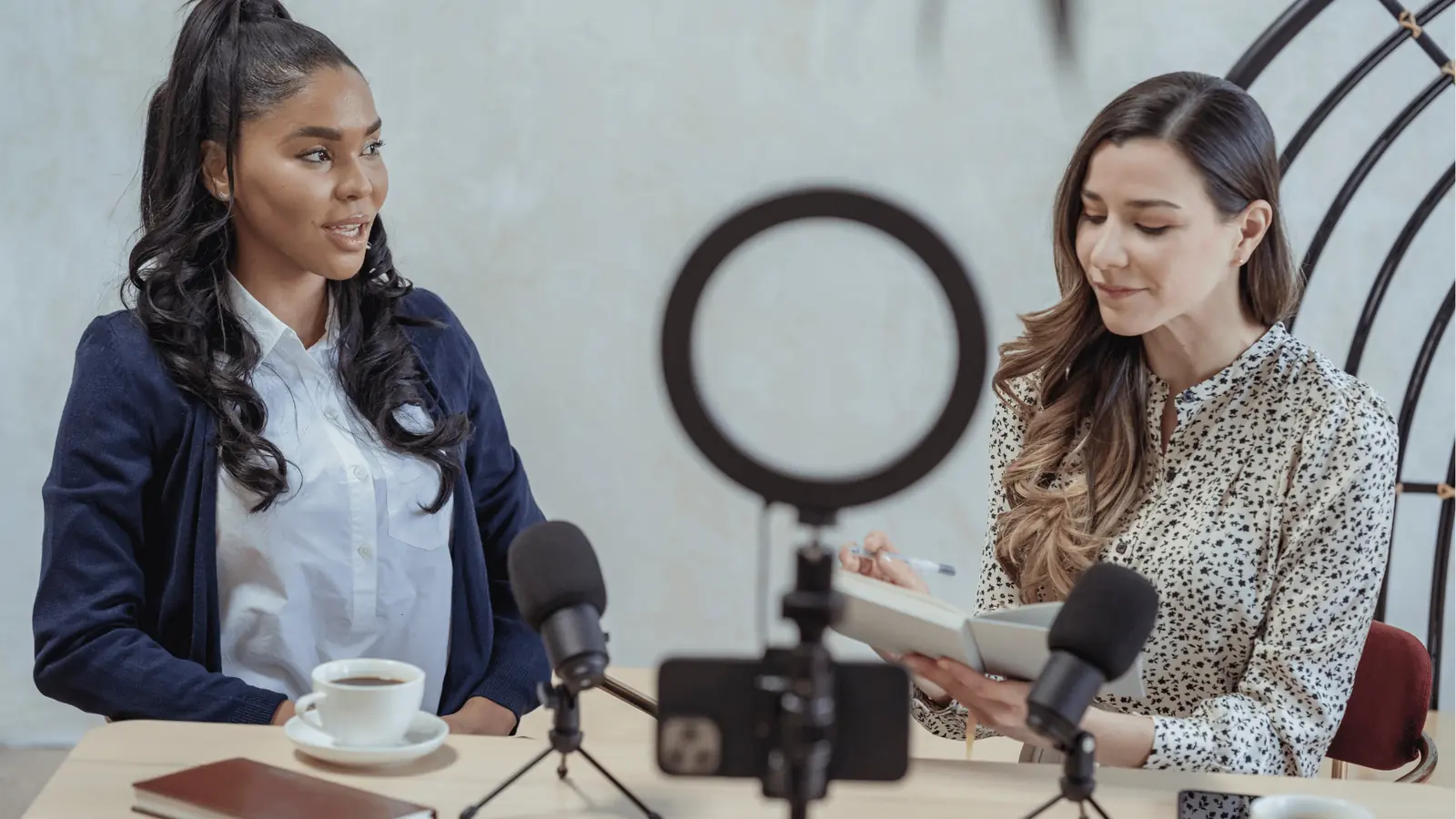 Two women recording a podcast at a table with microphones and ring light for community management