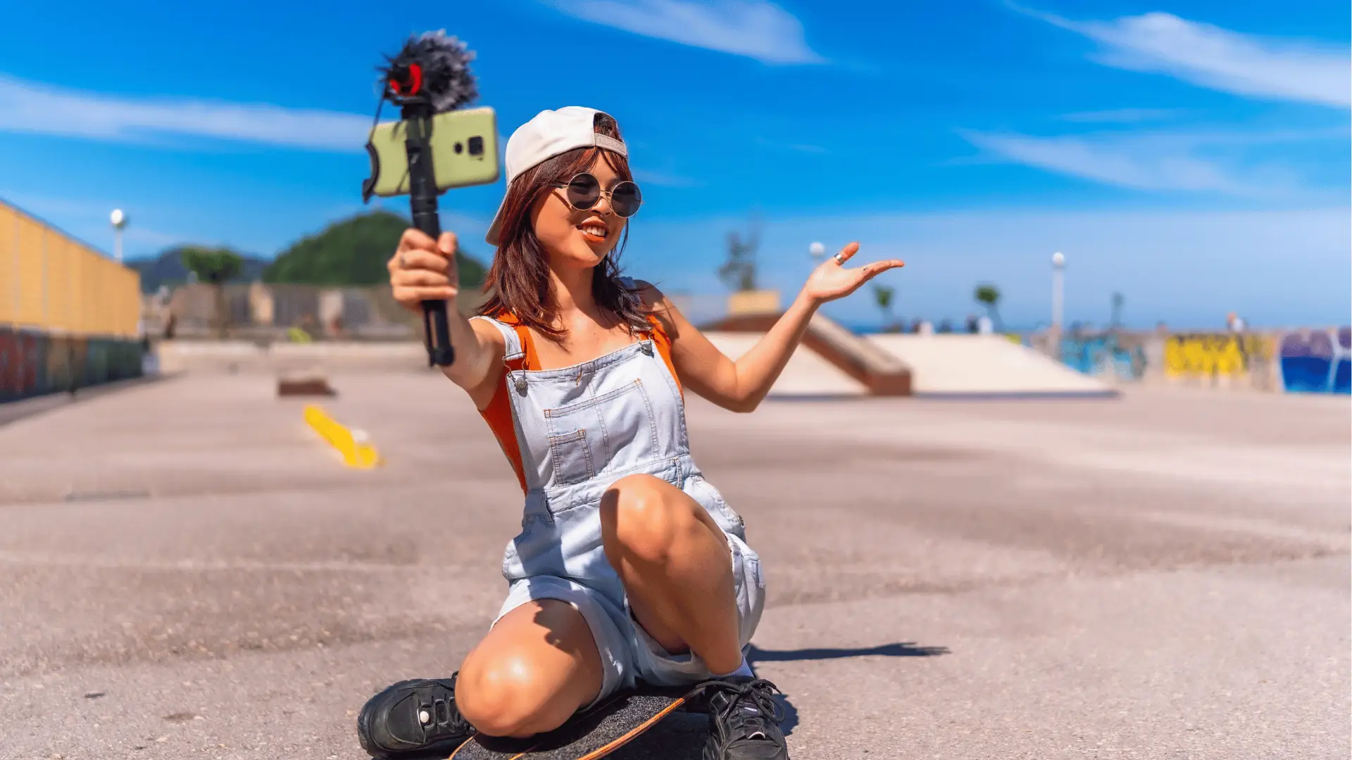 Young woman kneeling on skateboard vlogging with a smartphone mounted on a microphone