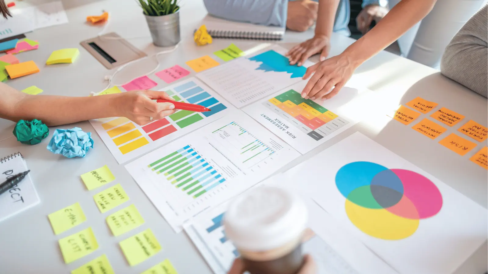 Hands pointing at colorful charts, sticky notes, and a Venn diagram on a desk for publishing