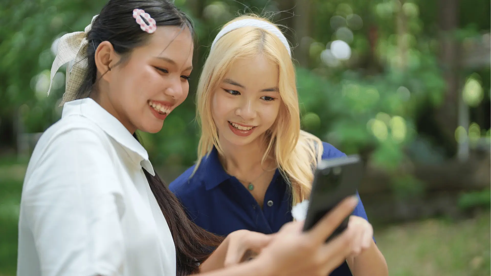 Two young women smiling and looking at a smartphone outdoors