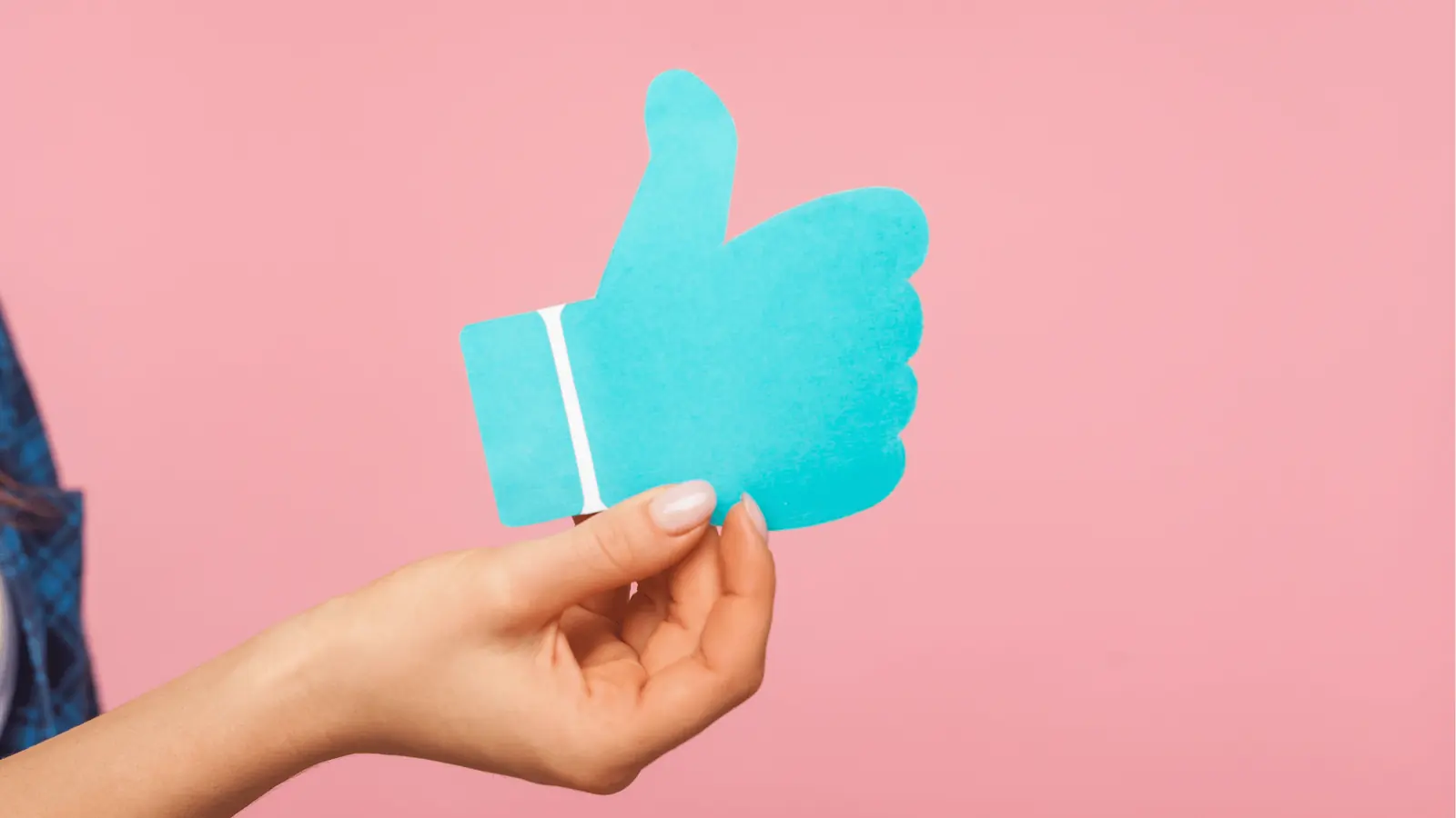 Hand holding blue paper thumbs up cutout against pink background for publishing