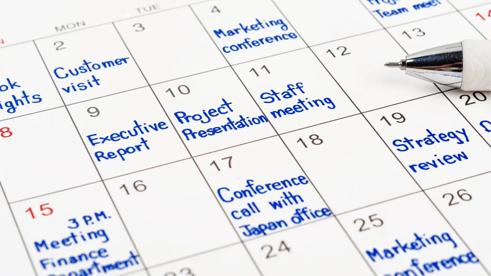 Close-up calendar page with handwritten blue appointment notes and pen for creative production